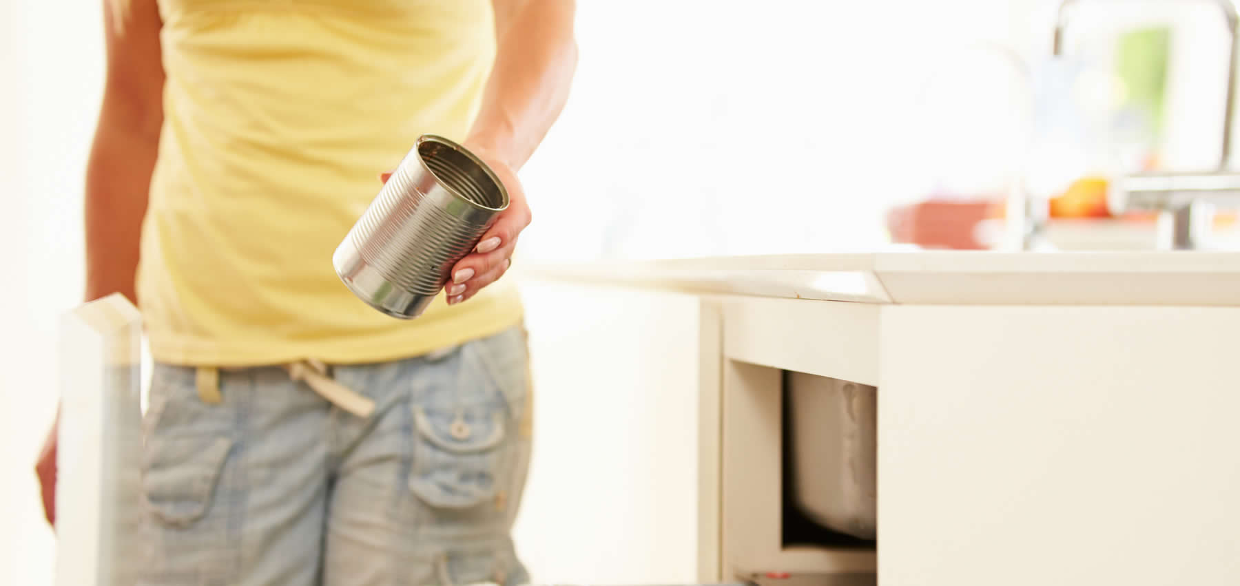 A person out of frame holds an empty aluminum food can in a kitchen. Indicates that they may be taking it off to recycle, promoting metal sustainability