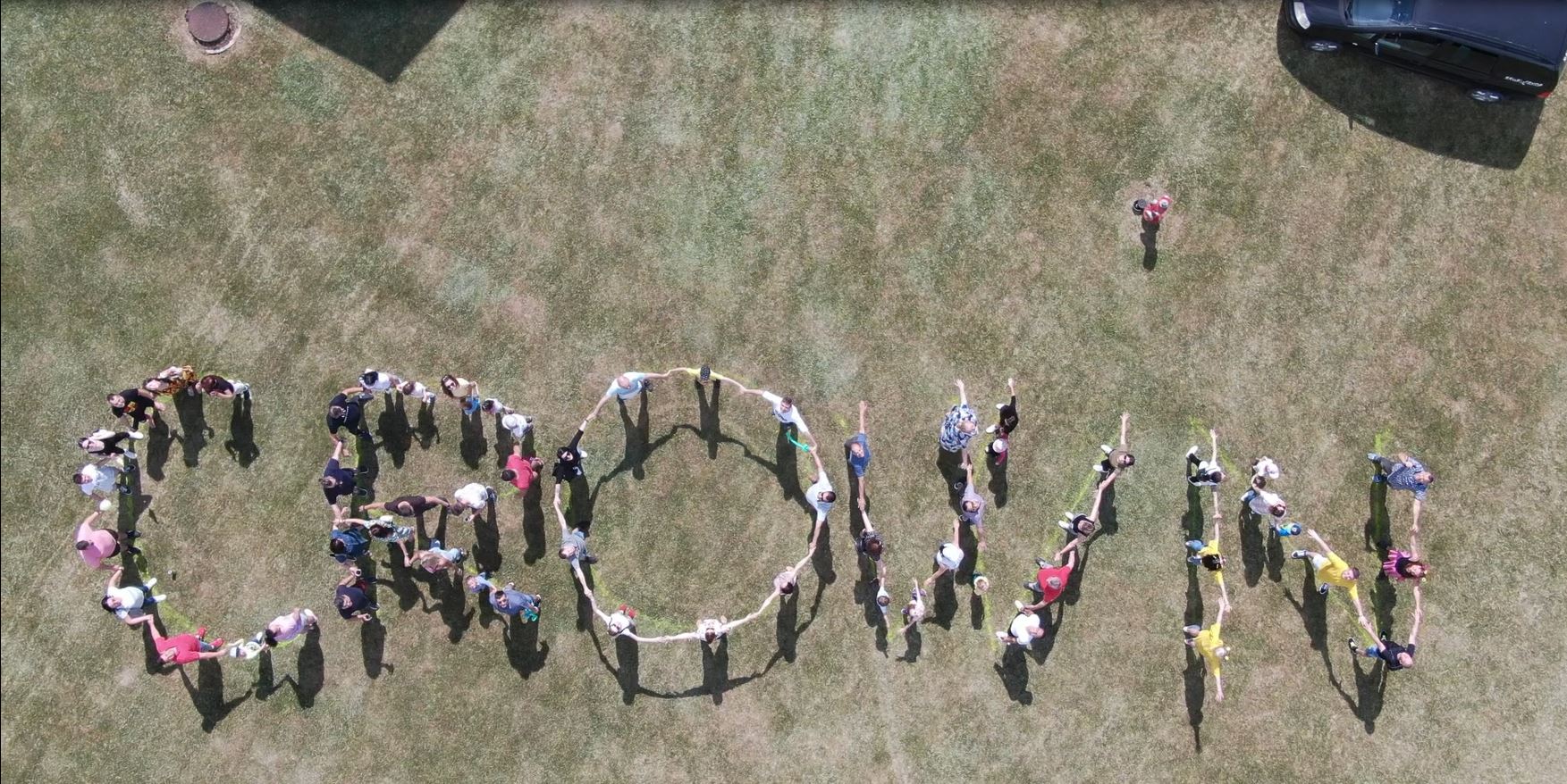 An arial shot of several people linking their arms together to form the word "Crown" 