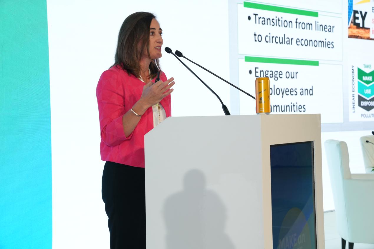 A female-presenting person in business dress stands behind a podium and speaks into a microphone at a conference.