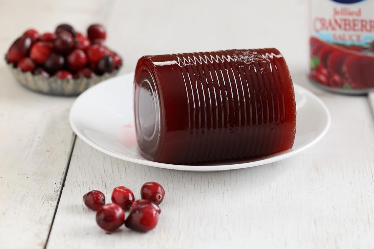 Red cranberry jelly from a can sitting upon a white place surrounded by cranberries.