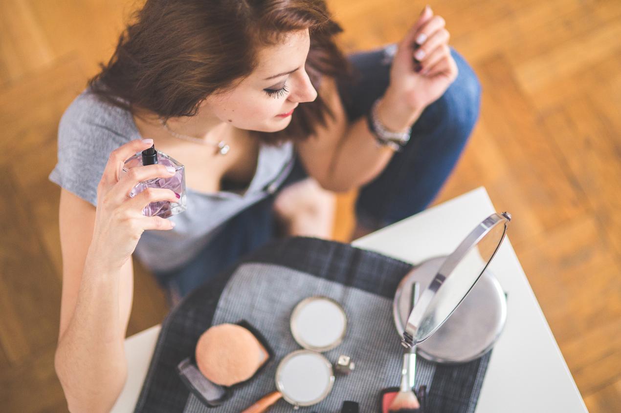A woman sitting at a table testing different perfumes,.