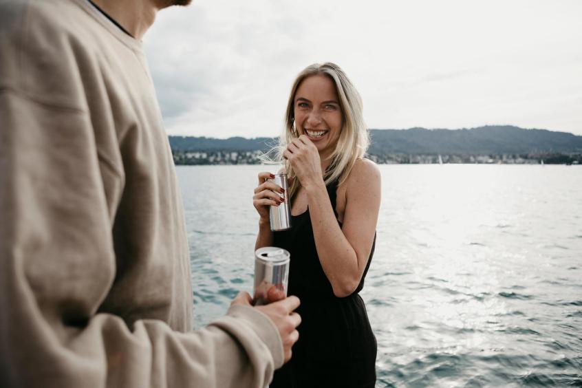 Blonde woman holding can with lake and hills in background